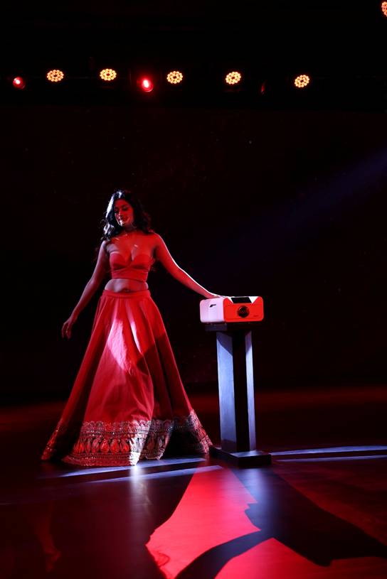 A woman in an elegant red gown stands confidently beside a product placed on a pedestal